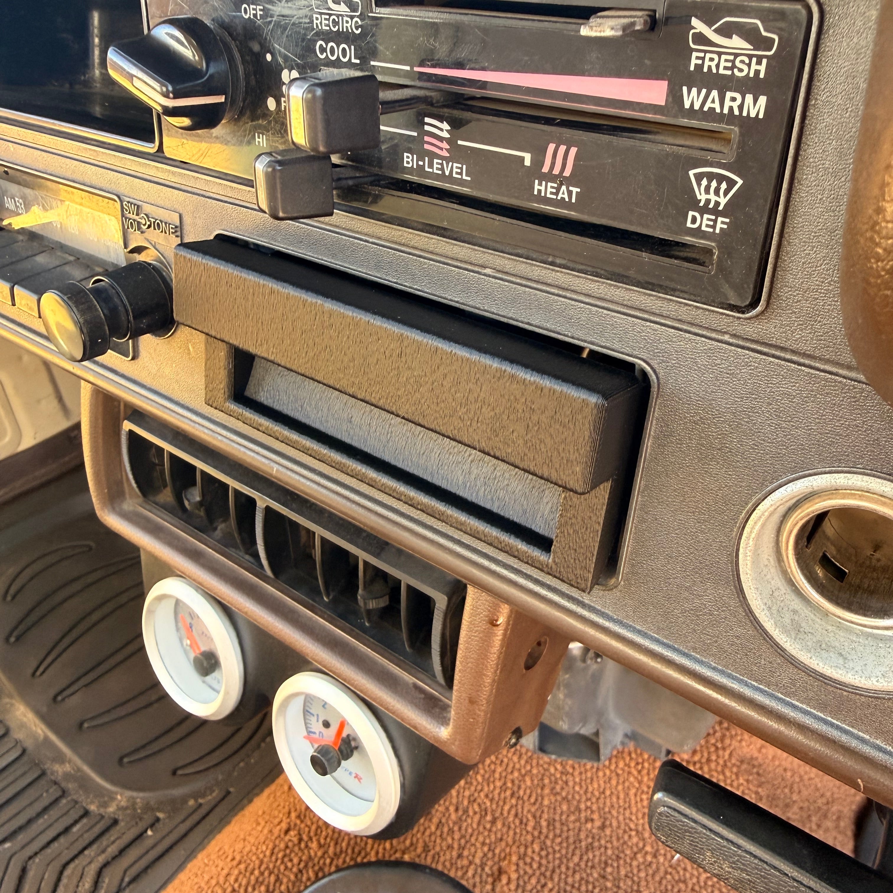 Close-up of a vintage car dashboard climate control panel with a cassette player slot, temperature gauges, and orange carpeted floor.