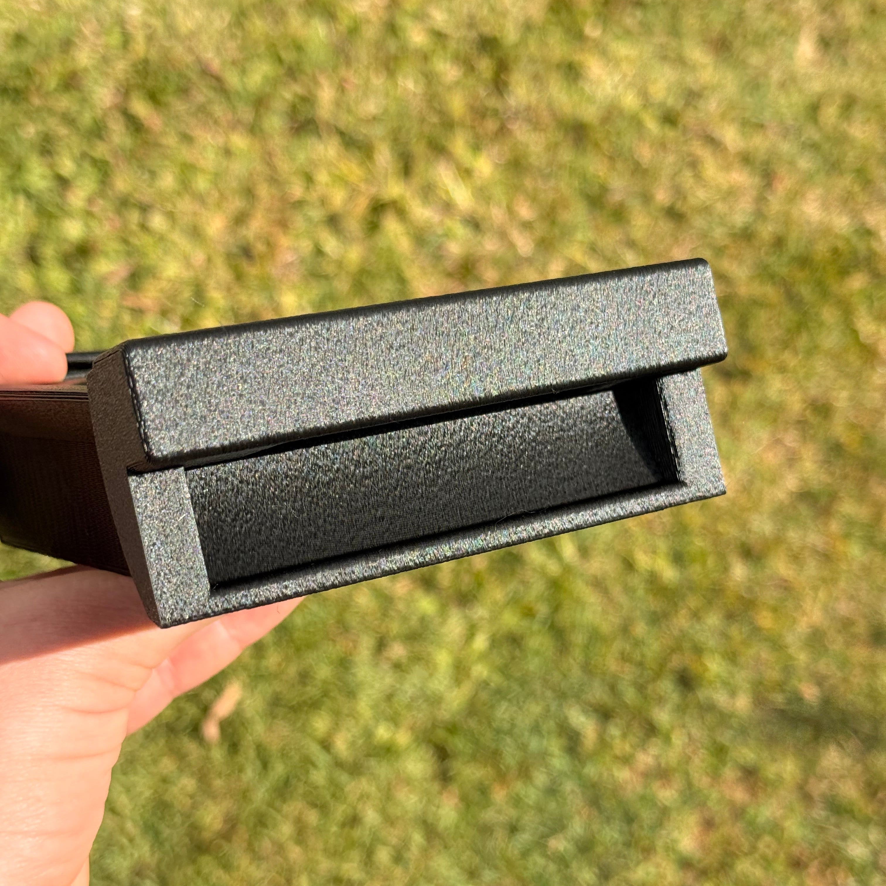 A close-up of a black textured rectangular component held by a hand against a blurred green grass background.