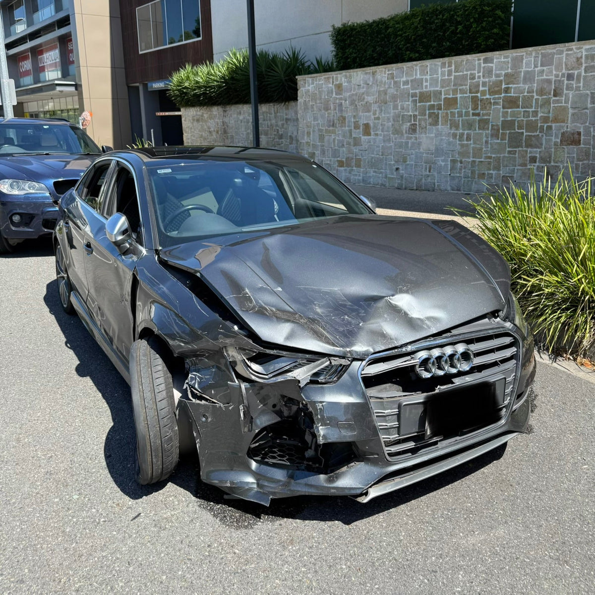 Wrecked Audi car in front of a building with 'Dan M' sign.